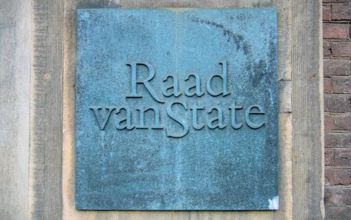 De foto toont een koper plaquette met daarop het logo van de Raad van State.