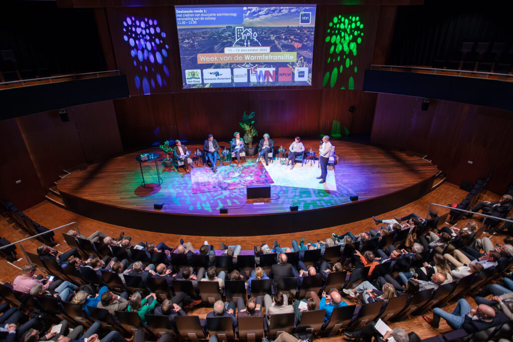 Foto van podium in Tivoli met sprekers en luisteraars in de zaal