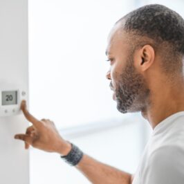 Een man kiest de temperatuur op de thermostaat. Een jonge, geconcentreerde man drukt op een knop van het verwarmingssysteem.