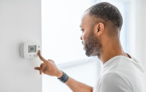Een man kiest de temperatuur op de thermostaat. Een jonge, geconcentreerde man drukt op een knop van het verwarmingssysteem.