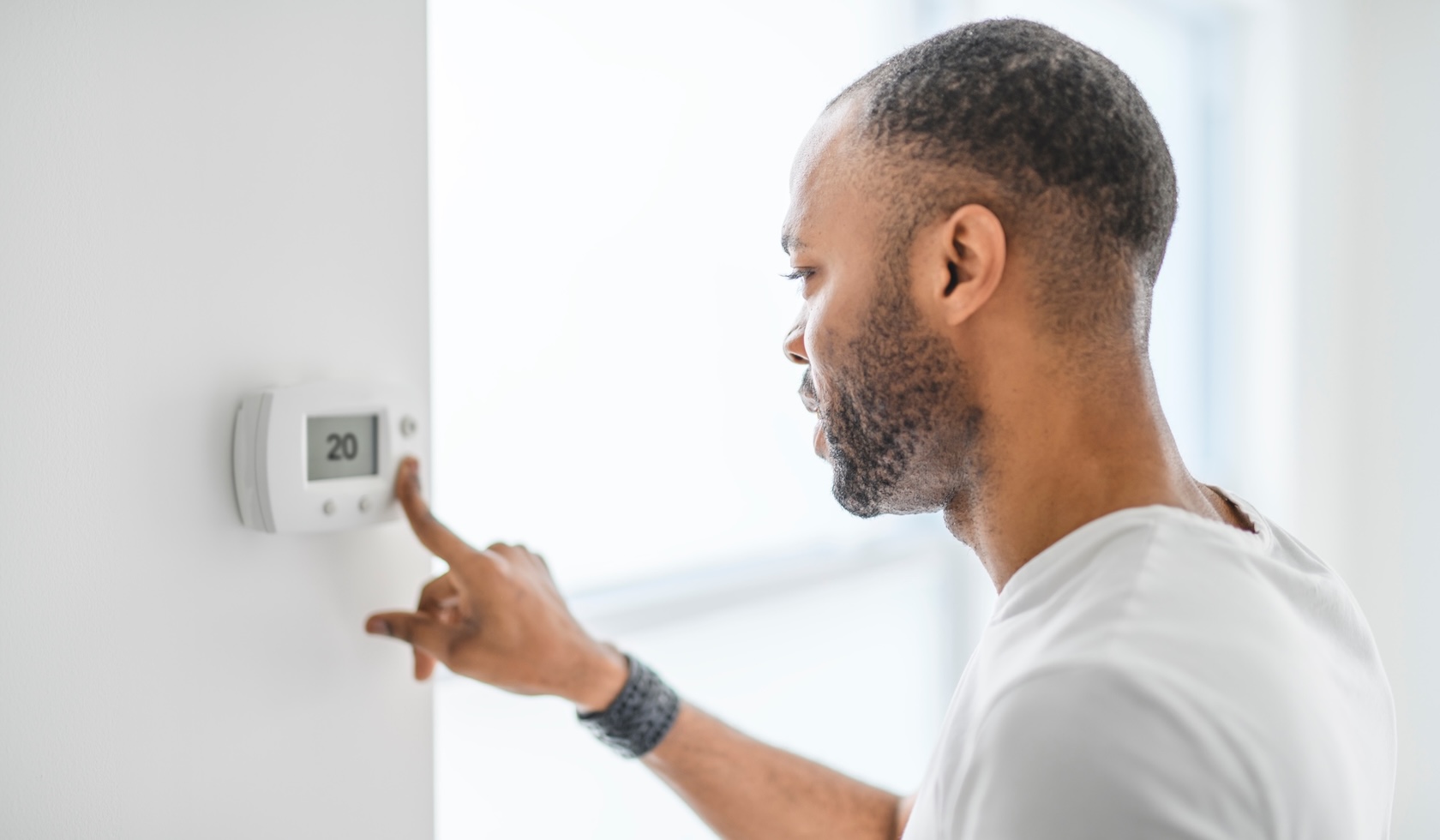 Een man kiest de temperatuur op de thermostaat. Een jonge, geconcentreerde man drukt op een knop van het verwarmingssysteem.