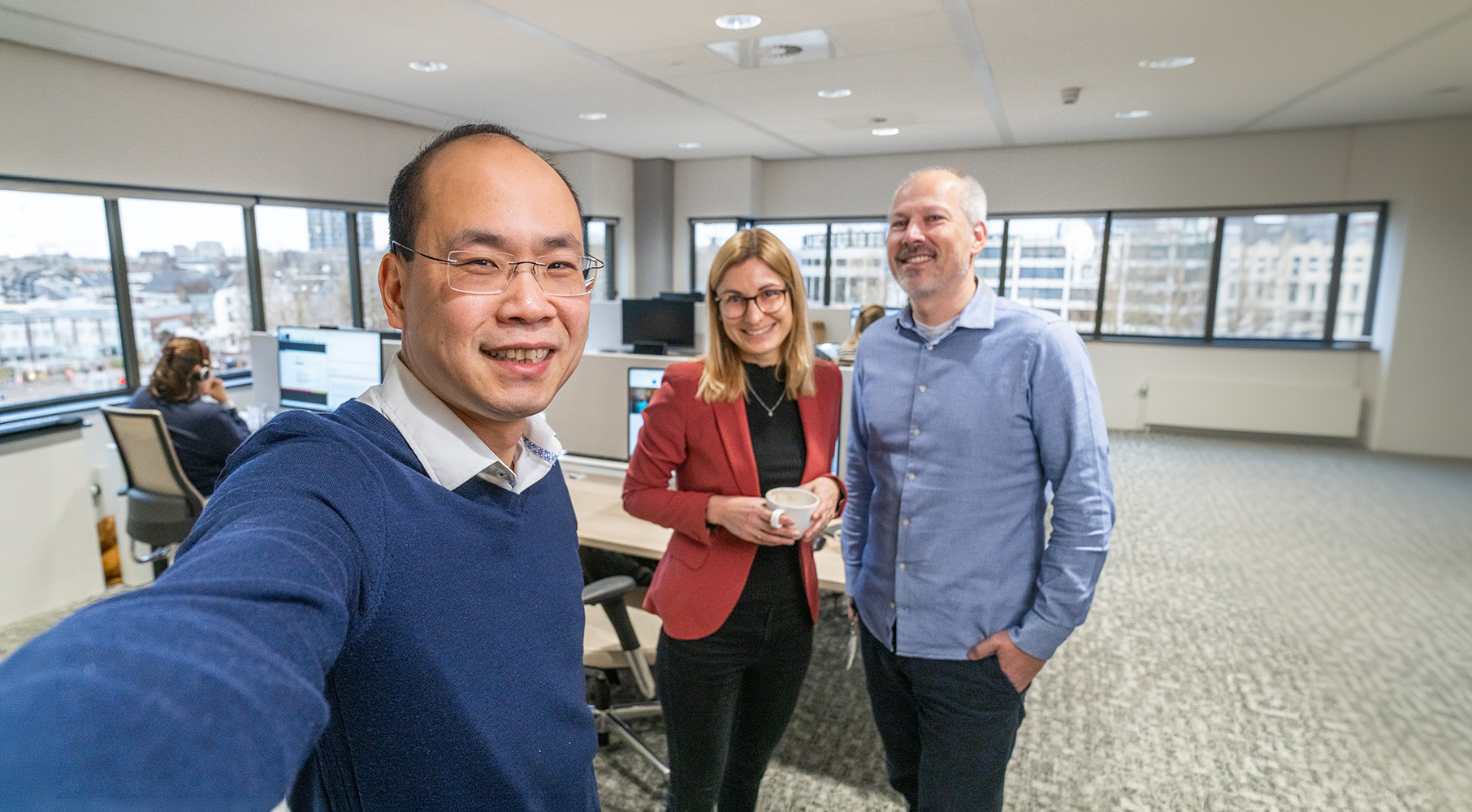 EBN-collega’s maken een selfie in een open kantoorruimte met werkplekken en uitzicht op de stad.